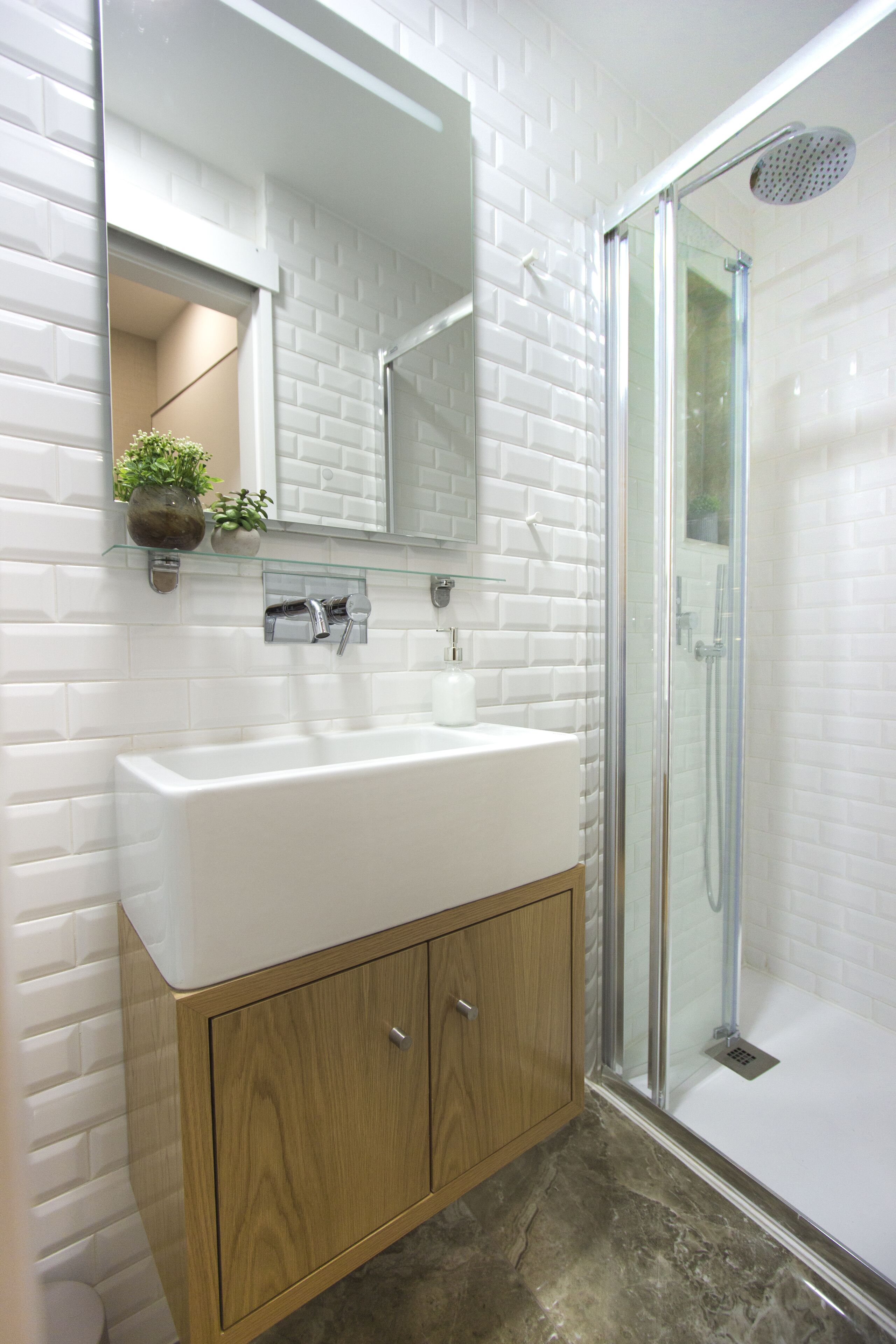 Une salle de bain moderne avec une douche à l’italienne aux carreaux blancs, un meuble-lavabo en bois avec un lavabo blanc et un miroir au-dessus du meuble.
