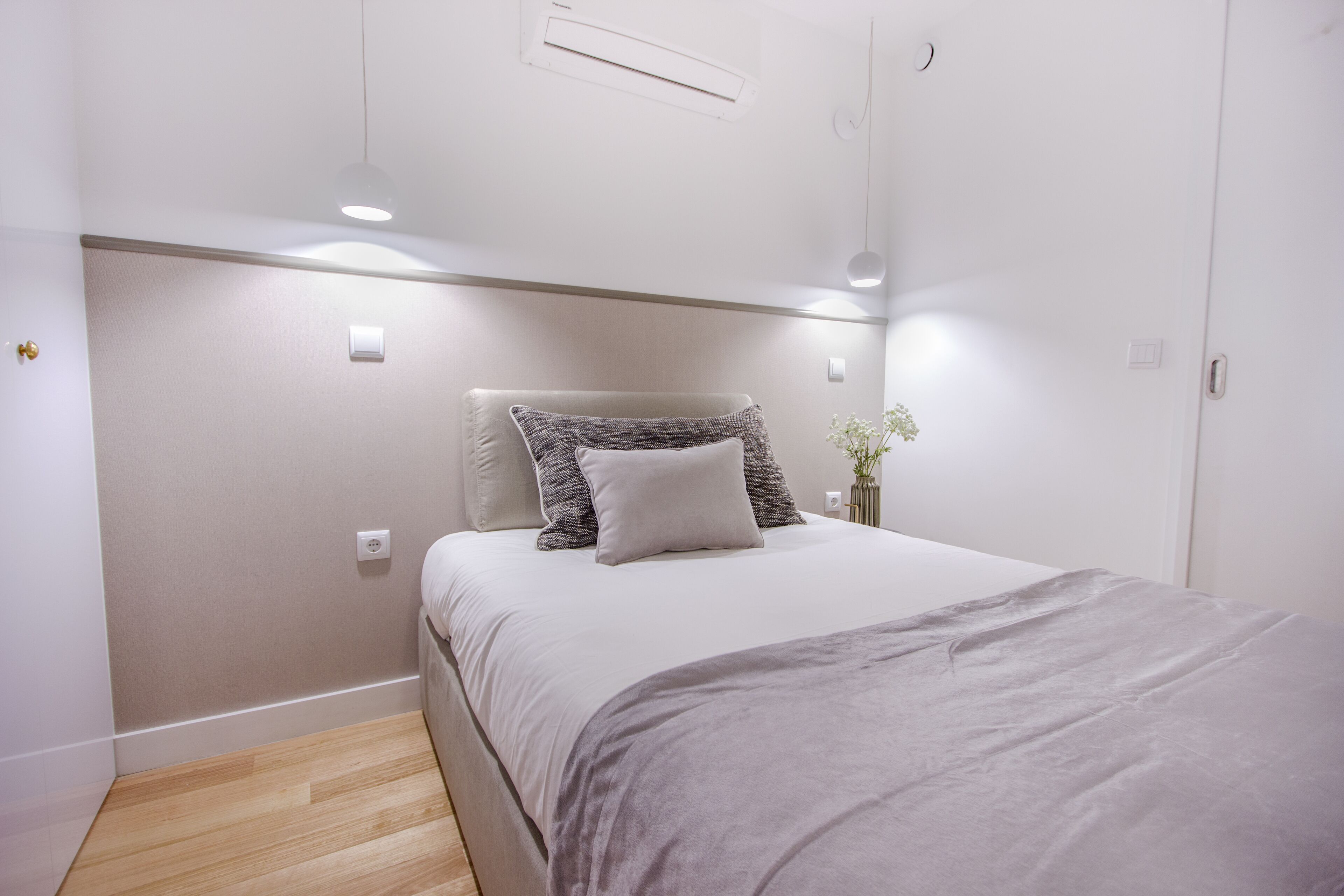 A bedroom with a bed, a bedside table, and a wall-mounted air conditioning unit.
