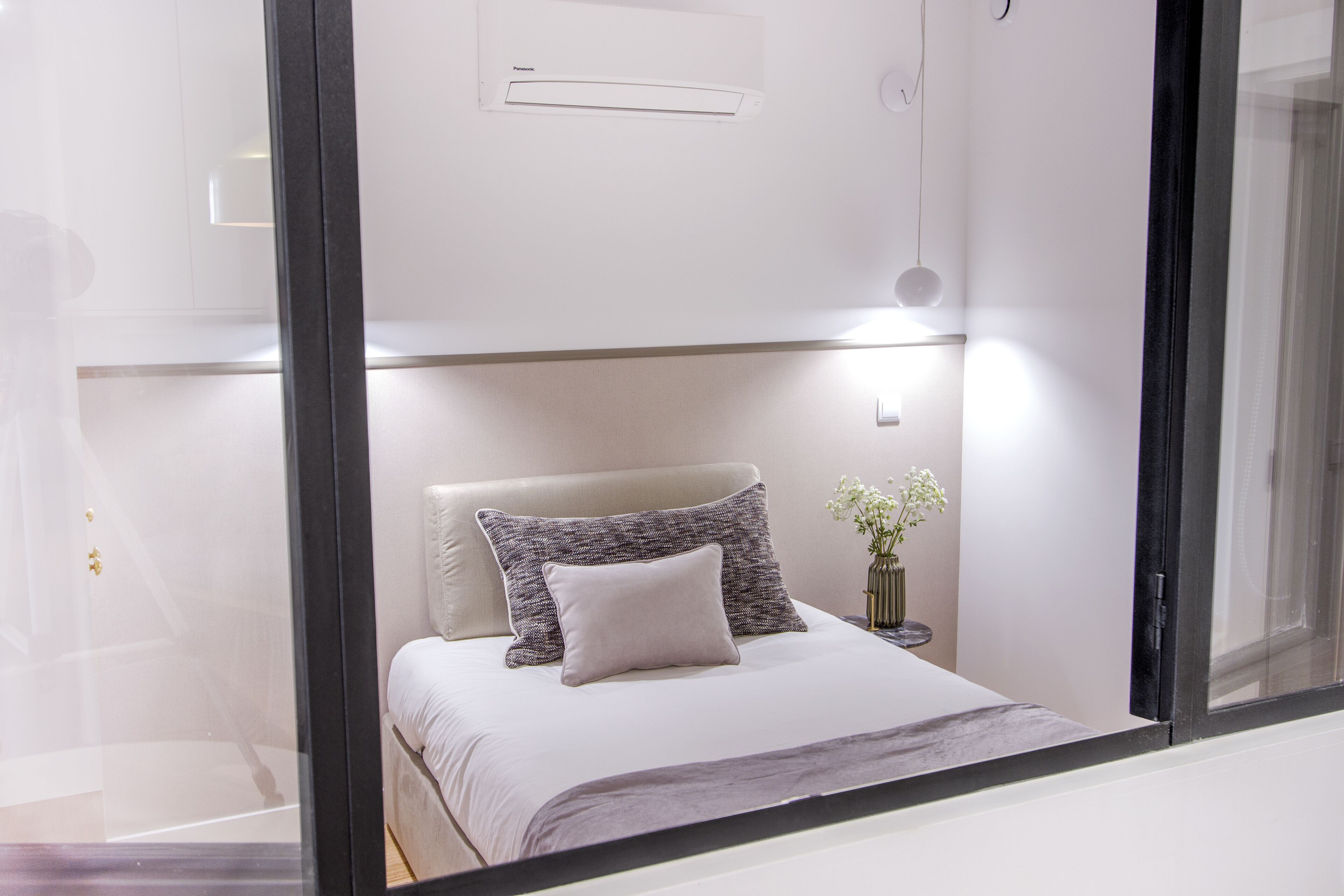 A modern bedroom with a bed, pillows, a nightstand, and a vase with flowers.