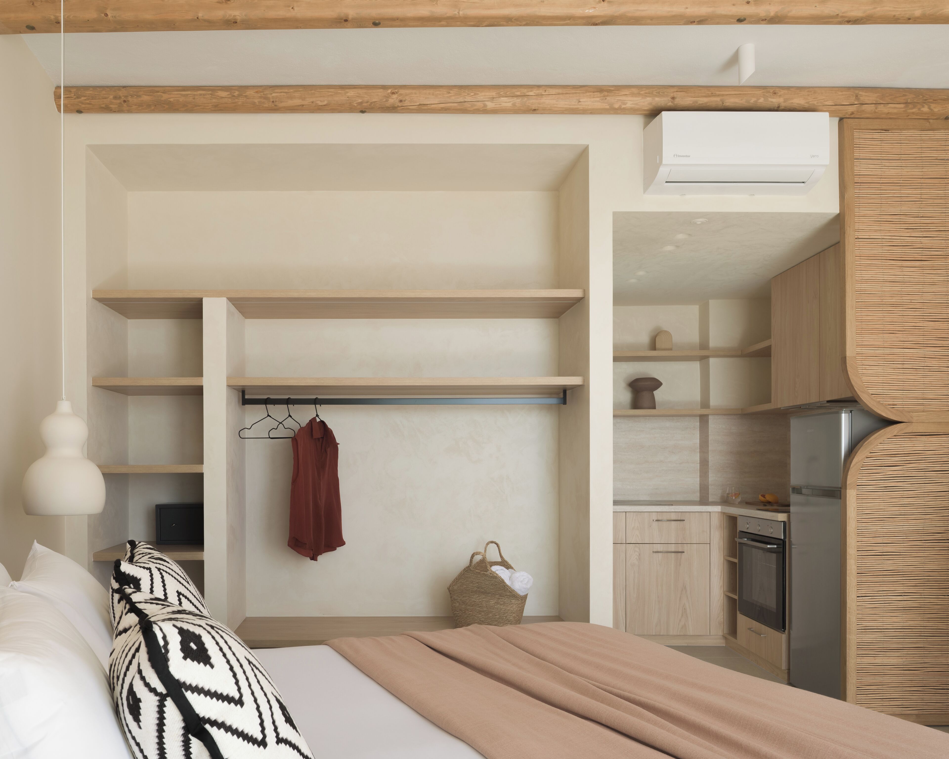 A modern bedroom with a bed, a hanging light fixture, a wardrobe, and a kitchenette.