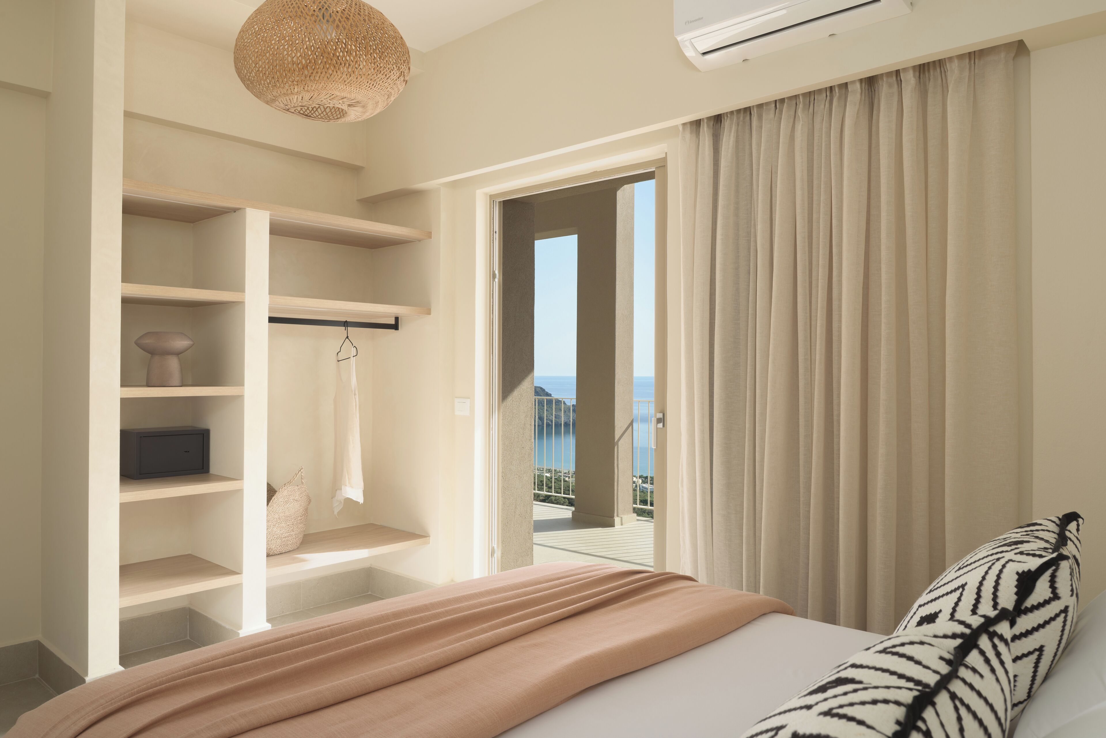 A bedroom with a bed, a closet with shelves, a hanging rack, and a view of the sea through a door.