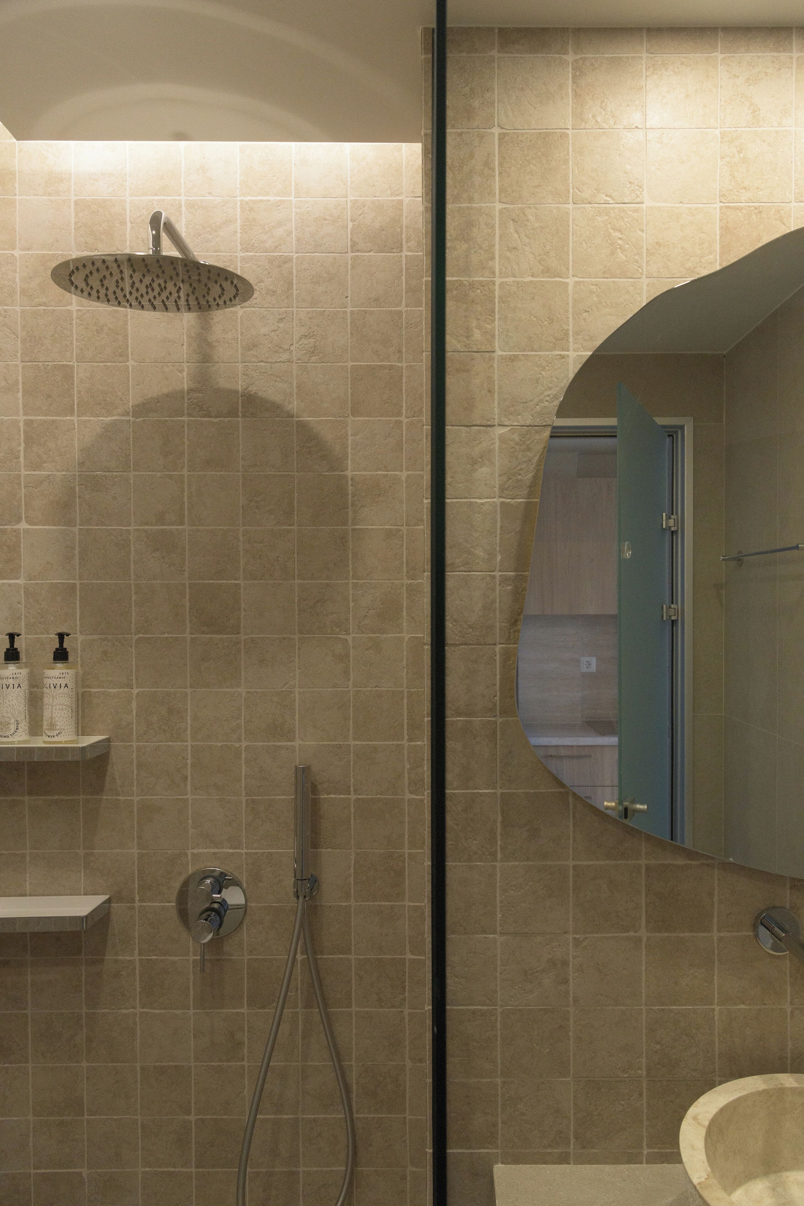 A bathroom with a shower, a sink, and a mirror. There are toiletries on a shelf.