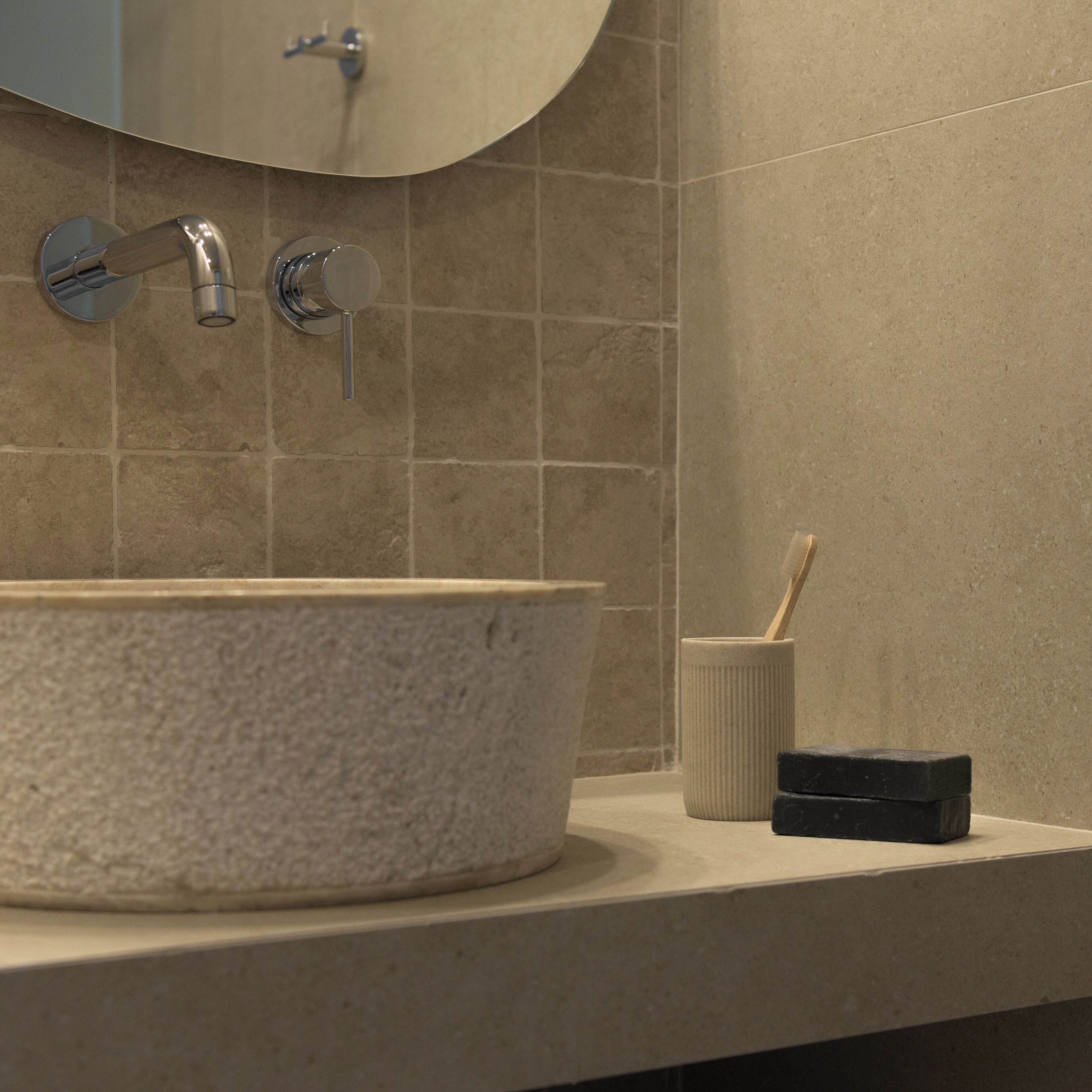 A bathroom with a round sink, a mirror, and a toothbrush holder.