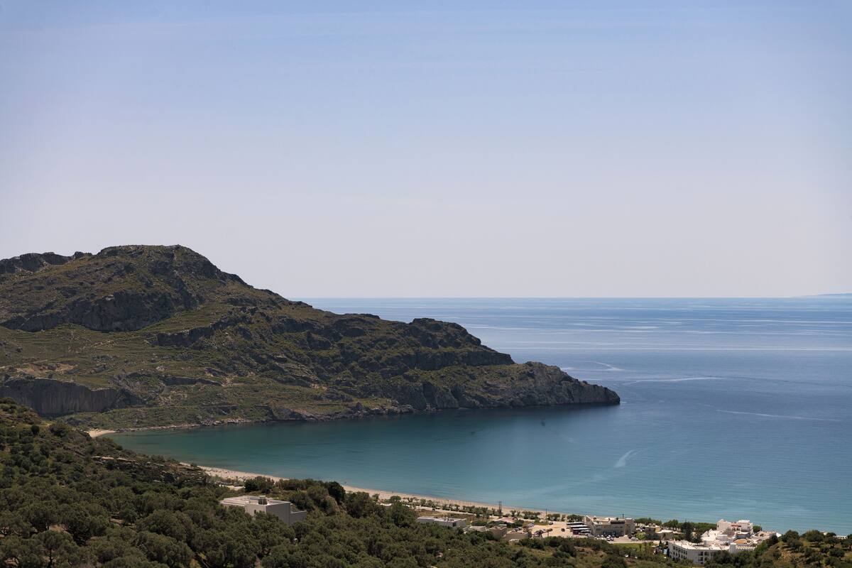 A coastal landscape with a mountain, beach, and buildings.