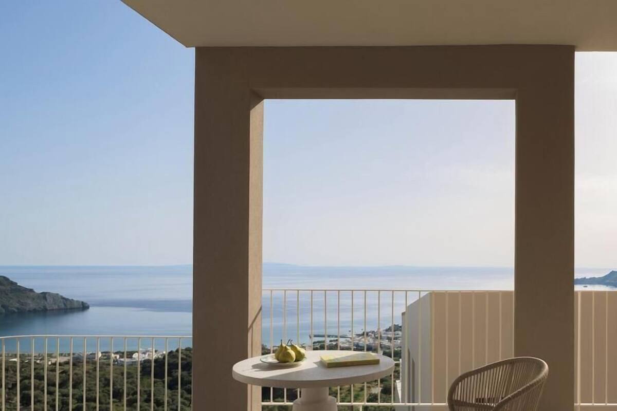 A balcony with a view of the sea, a table with fruit, and a chair.