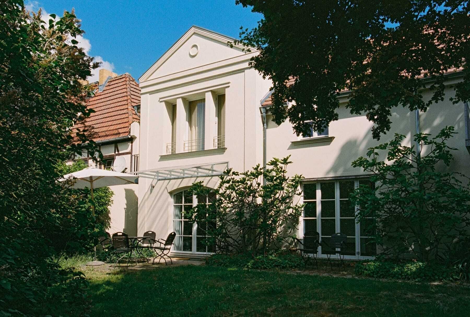 A white building with a triangular pediment, large windows, and a covered patio area with outdoor seating.