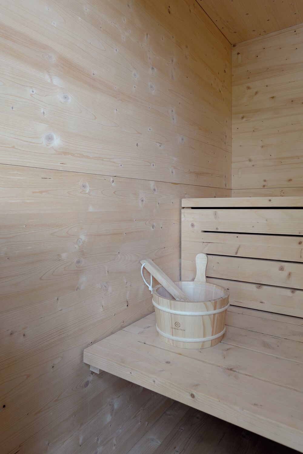 Uma sauna de madeira com um balde e um pilão de madeira numa prateleira.