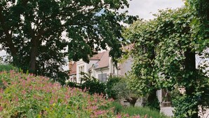 A garden with flowering plants and a house with a tiled roof. - REMISE LOFT: Spacious apartment with balcony, loggia window and water access (Werder (Havel))