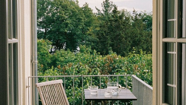 A wooden deck with two chairs and a small table, overlooking a lush garden. - REMISE LOFT: Spacious apartment with balcony, loggia window and water access (Werder (Havel))