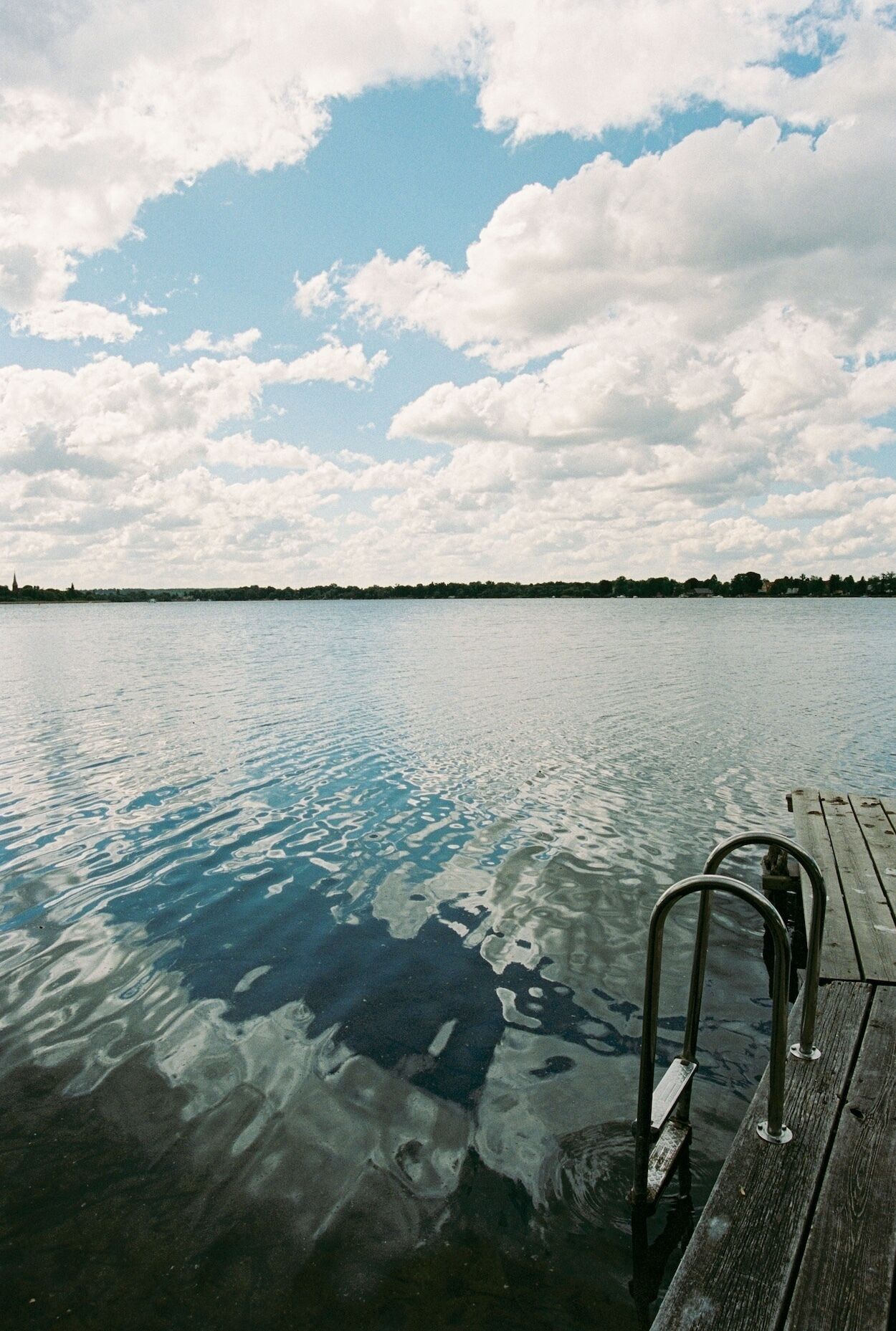 Eine hölzerne Mole, die in ruhiges Wasser führt, mit blauem Himmel darüber.