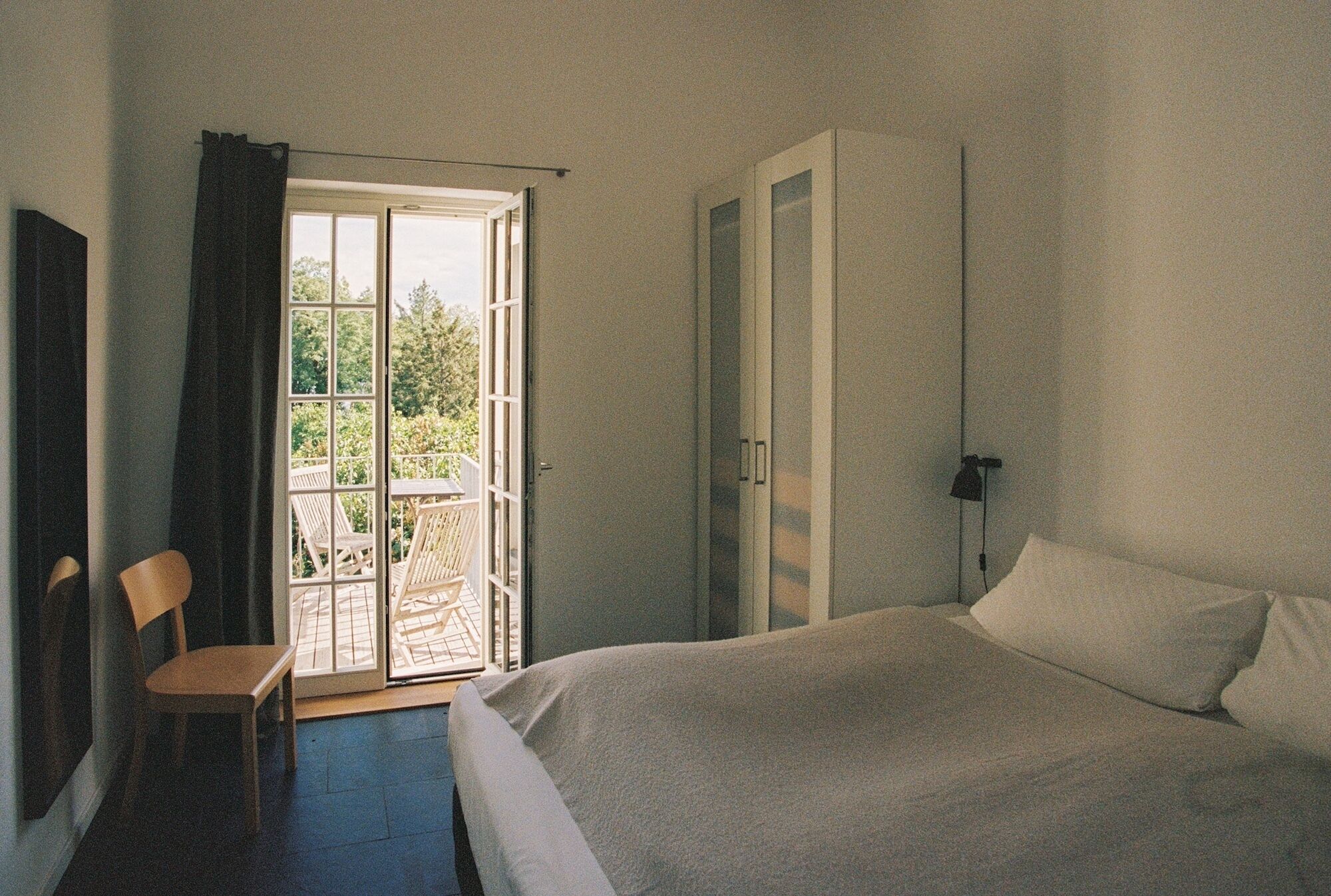 Un dormitorio con cama, una silla, un armario y una puerta corredera de vidrio que da a un espacio exterior con sillas.