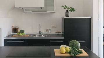 A modern kitchen with a black countertop, stainless steel sink, and a black refrigerator. There are wooden cutting boards with fruits and vegetables on the counter.