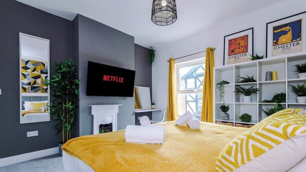 A modern bedroom with a bed, a TV, a bookshelf, and a window with curtains. - Stylish & Spacious home, Great Location, sleeps 6! (Chester)