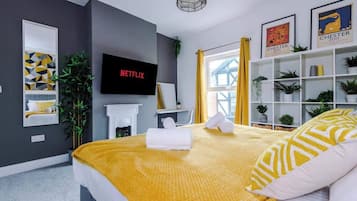 Um quarto moderno com cama, televisão, estante de livros e janela com cortinas.