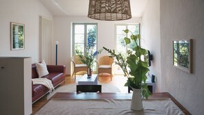 Un salon avec un canapé rouge, une table basse et une grande plante. Il y a deux fauteuils et un lampadaire.