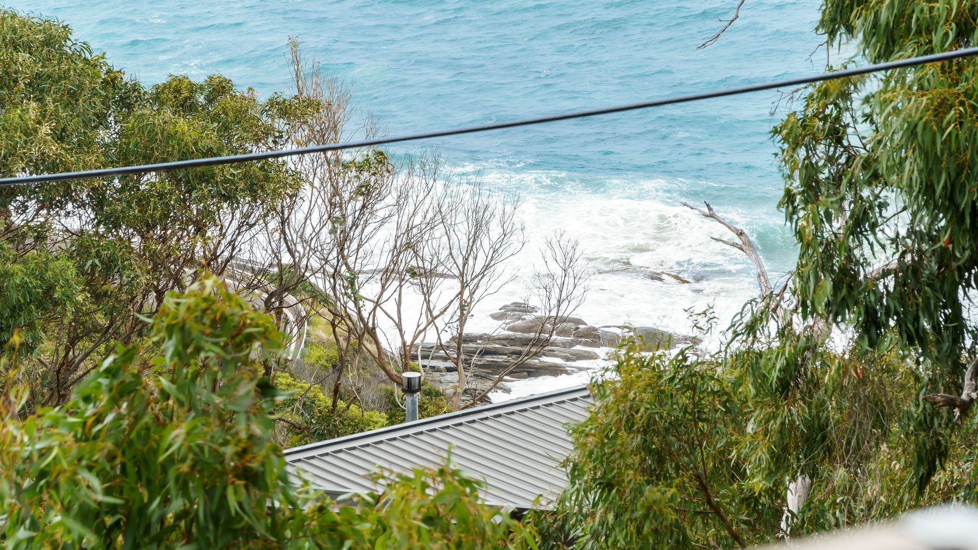 A coastal view with rocky shoreline, vegetation, and a building with a sloped roof.