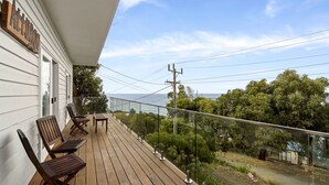 A wooden deck with two chairs and a table, overlooking a coastal area with trees and a view of the sea. - Attunga - Relaxed family beach home among the gum trees (Wye River)