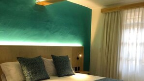 A modern hotel room with a large bed, teal accent walls, and a wooden headboard. - Pinoli House, Xochimilco Neighborhood (Oaxaca)