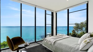 A bedroom with a large window overlooking the sea, a bed, a chair, and a small table.