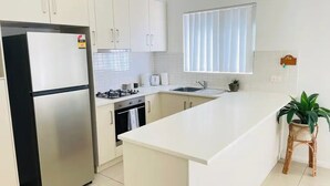 Eine moderne Küche mit weißen Schränken, einem Edelstahlkühlschrank, einem Gasherd und einer Spüle.