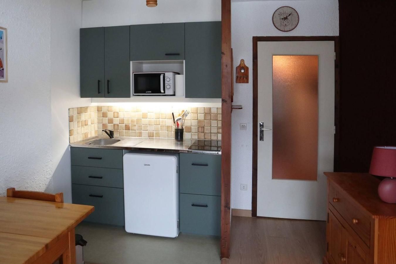 Une cuisine compacte équipée d’un four à micro-ondes, d’un petit réfrigérateur et d’un plan de travail recouvert de carreaux.