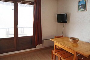 Una habitación con una mesa y sillas de madera, un televisor montado en la pared y una ventana con cortinas.