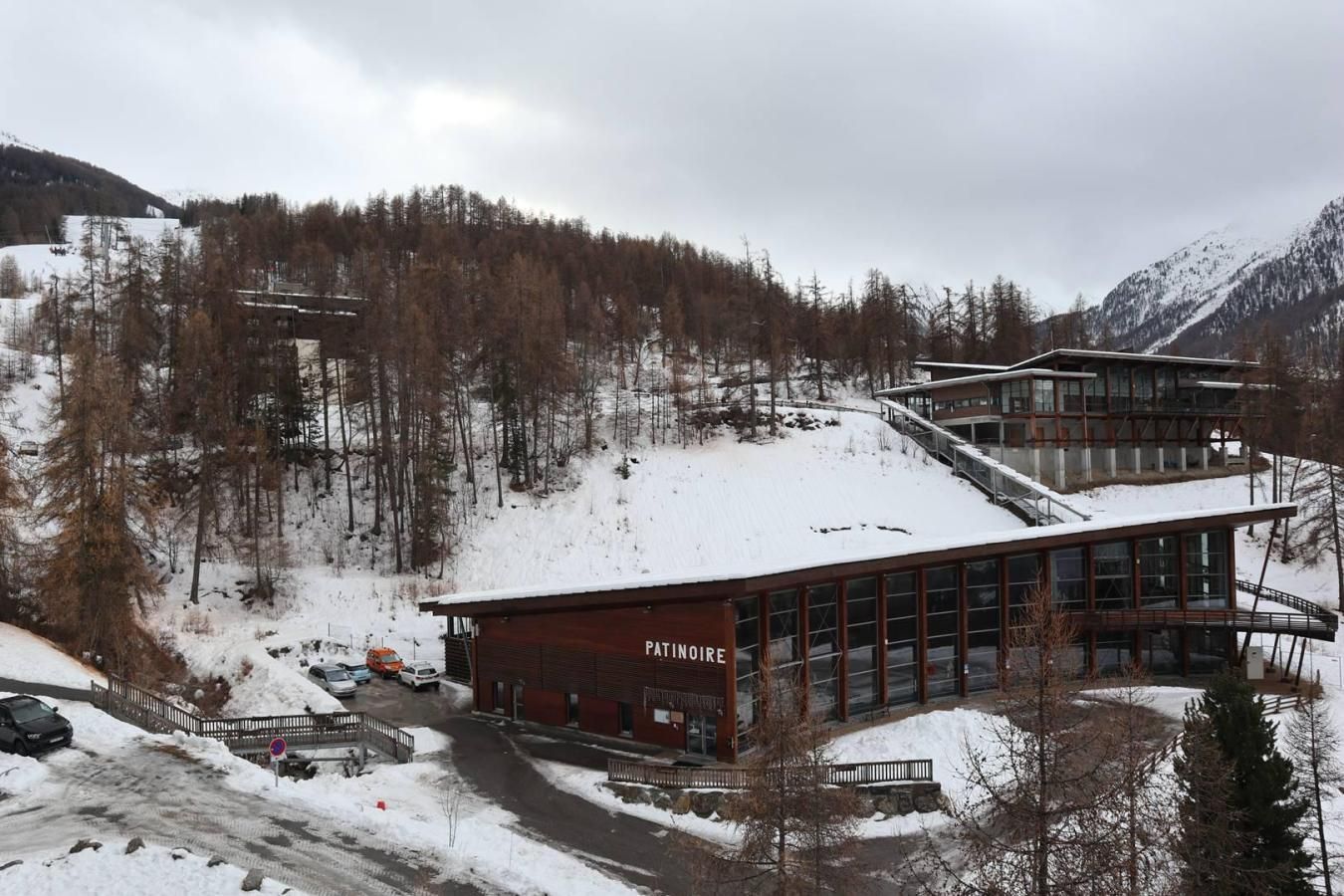 A modern building with a sign reading 'PATINOIRE' in a snowy mountainous area.