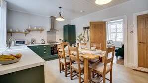 Une cuisine moderne avec un coin repas, comprenant un plan de travail blanc, des chaises en bois et un meuble vert.
