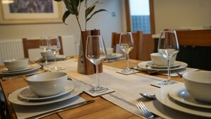 Une table à manger dressée avec des bols, des assiettes et des verres à vin blancs, et une plante placée au centre.