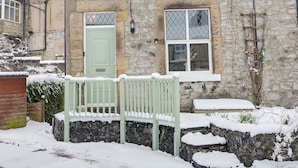 Un bâtiment en pierre avec une porte verte, une fenêtre ornée d’un motif en treillis et un banc devant.