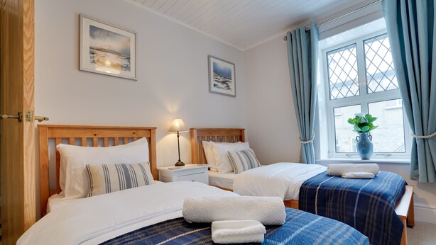 Une chambre double avec deux lits, une table de chevet, une lampe et une fenêtre avec des rideaux.