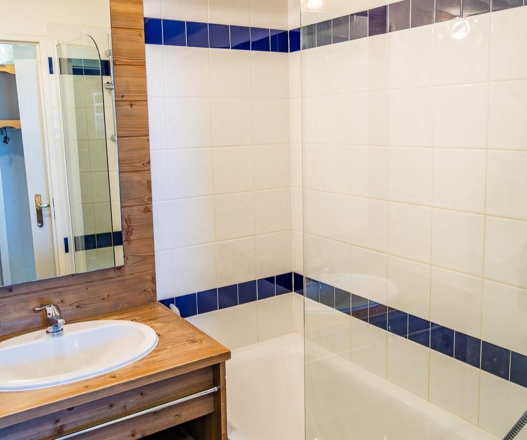 A bathroom with a wooden vanity, a sink, a mirror, and a shower area with blue-tiled walls.