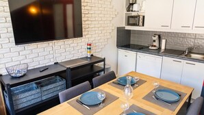 A modern kitchen with white cabinets, a black countertop, and a flat-screen TV mounted on a white brick wall.