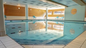 An indoor swimming pool with tiled floors, wooden panel walls, and blue lounge chairs.
