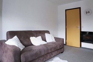 A living room with a brown sofa, three white pillows, a white fluffy rug, and a wooden door.