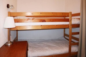 A bunk bed with a wooden frame, a bedside table with a lamp, and a wall-mounted light fixture.