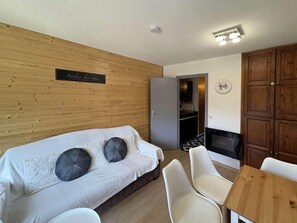 A cozy room with a wooden wall, a white sofa with two pillows, a small table, and a fireplace.