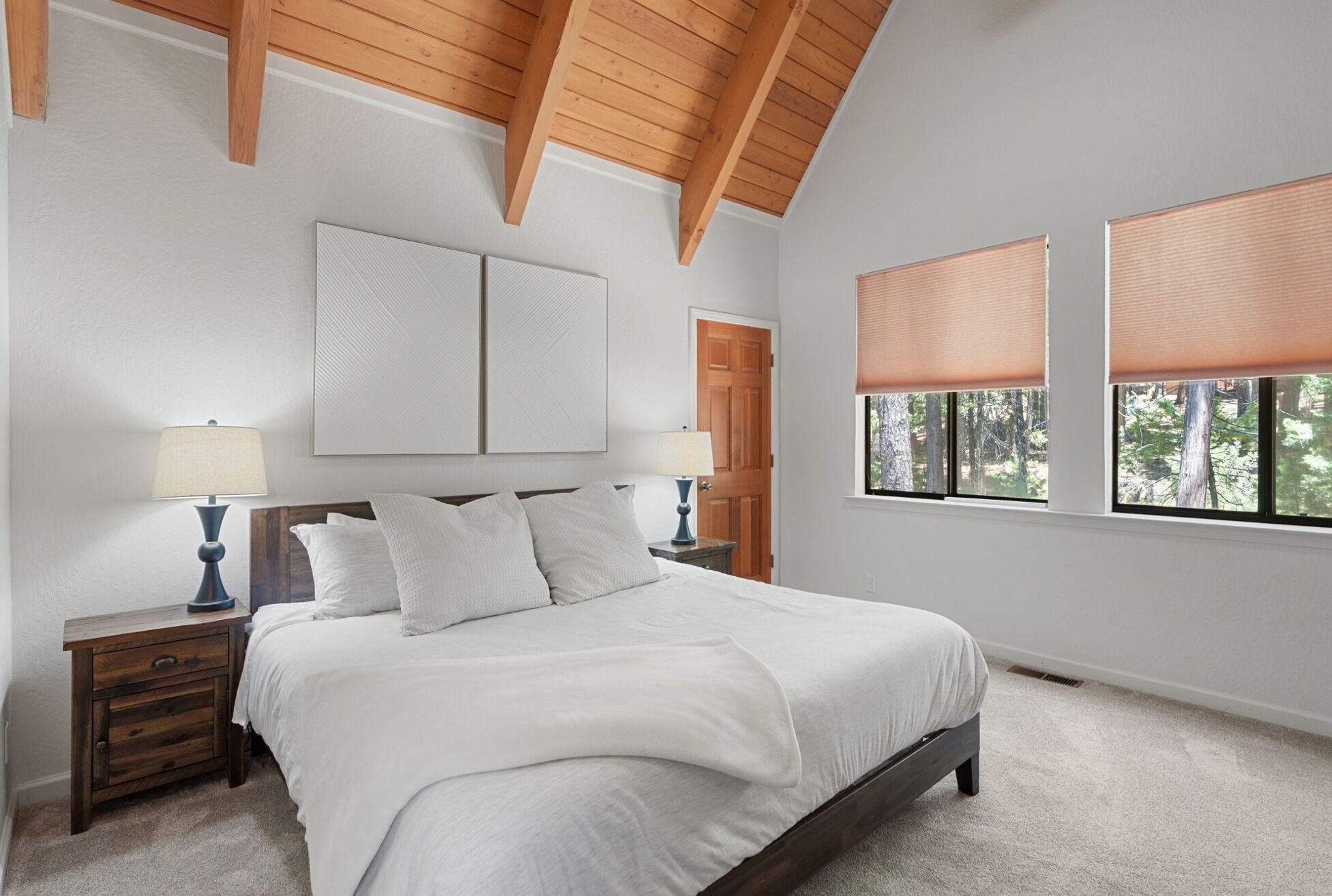 A bedroom with a bed, two bedside tables, a wooden ceiling, and a window with blinds.