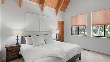 A bedroom with a bed, two bedside tables, a wooden ceiling, and a window with blinds.