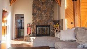 A cozy living room with a stone fireplace, a wooden ceiling, and a large gray sofa.