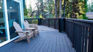A wooden deck with three Adirondack chairs and a glass door leading to a room.