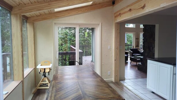 A spacious kitchen with a large wooden table, a stone accent wall, and a view of the outdoors.