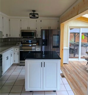 A modern kitchen with white cabinets, a stainless steel refrigerator, a microwave, an oven, and a black countertop.