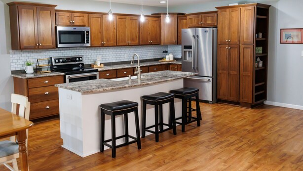 Una cocina moderna con armarios de madera, electrodomésticos de acero inoxidable, encimera de granito y una isla central con taburetes.