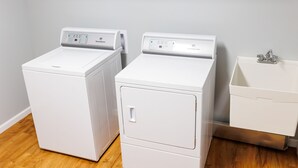 Dos lavadoras blancas de carga frontal junto a un lavabo blanco en un cuarto de lavado con piso de madera.