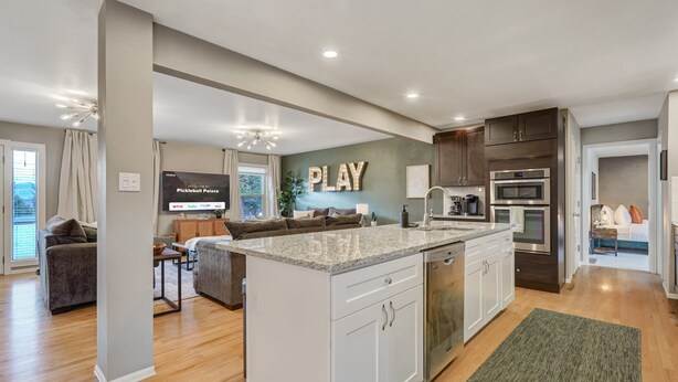 A modern kitchen with a central island, built-in appliances, and a dining area with a couch and table. - Pickleball Palace! 3 Courts | Game Room | Hot Tub (Colorado Springs)