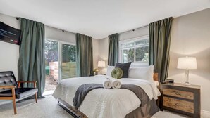 A bedroom with a bed, two bedside tables, a chair, and a window with curtains. - Pickleball Palace! 3 Courts | Game Room | Hot Tub (Colorado Springs)