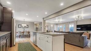 A modern kitchen with white cabinets, a central island, and a dining area with chairs and a table. - Pickleball Palace! 3 Courts | Game Room | Hot Tub (Colorado Springs)