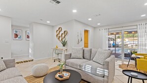Ein modernes Wohnzimmer mit einem grauen Sofa, einem runden Couchtisch und einem gelben Sessel. Eine Glastür führt zu einem Balkon mit einem Pool.