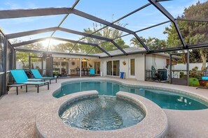 A covered outdoor swimming pool with lounge chairs, a hot tub, and a patio area with a view of the surrounding landscape.